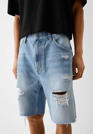 Shorts di denim azzurro chiaro con orli sfilacciati e diverse toppe consumate. Dotati di chiusura con bottoni e classico design a cinque tasche.