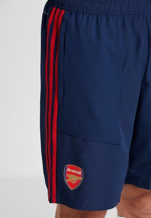 Shorts de sport bleu marine avec des rayures latérales rouges, taille élastique et patch logo Arsenal. Fabriqués à partir d'un tissu lisse et léger.