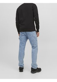 Felpa nera, jeans azzurri chiari con molte tasche, indossati con scarpe da ginnastica nere. Design semplice, vestibilità casual, senza motivi o dettagli visibili.