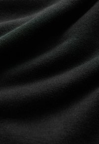 Gros plan sur un tissu noir doux avec des plis subtils et une texture fine en maille sous un éclairage doux.