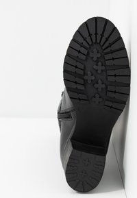 Bota de cuero negro con una superficie texturizada. Suela de goma resistente con un diseño de banda cruzada para una mejor tracción. Detalle de cremallera lateral.