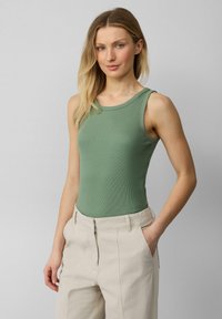 Groene geribde tanktop met een ronde halslijn, gecombineerd met lichtbeige hoge taillebroeken. De top heeft een aansluitende snit.