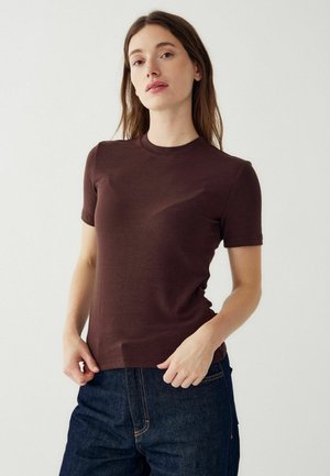 Rjava kratka majica s kratkimi rokavi in okroglim izrezom, gladke teksture in prilegajočega kroja, v kombinaciji s temnimi kavbojkami.