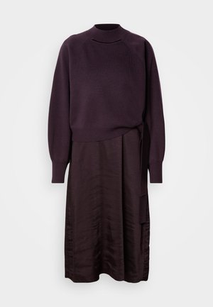 Violetā kleita ar adītu augšu, kurai ir augsts kakls un garas piedurknes, kā arī zīda līdzīga svārka ar sasienamu detaļu jostasvietā.