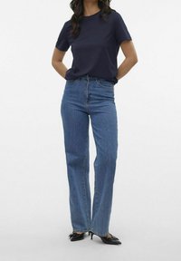 Granatowa koszulka z okrągłym dekoltem w połączeniu z błękitnymi spodniami o prostym kroju z wysokim stanem. Do stroju dodano czarne buty na obcasie.