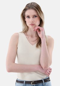 Beige gerippter Tanktop mit V-Ausschnitt, schmaler Passform und breiten Schulterträgern, kombiniert mit hellblauen Jeans und einem braunen Gürtel.
