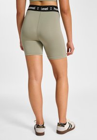 Zielone szorty poliestrowe z czarnym pasem, na którym znajduje się logo "Hummel". Szorty mają gładką, elastyczną teksturę i dopasowany krój.