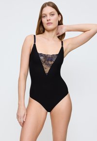 Czarny jednoczęściowy strój kąpielowy z głębokim dekoltem w serek, ozdobiony przezroczystymi koronkowymi detalami na klatce piersiowej oraz regulowanymi ramiączkami dla idealnego dopasowania.