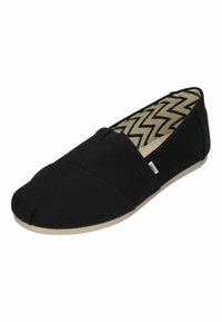 Scarpa in tela nera scivolosa con suola beige e motivo a zigzag sulla soletta imbottita.