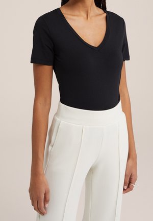 Body nero a maniche corte con scollo a V abbinato a pantaloni bianchi a vita alta, caratterizzati da una texture liscia e pieghe delicate.