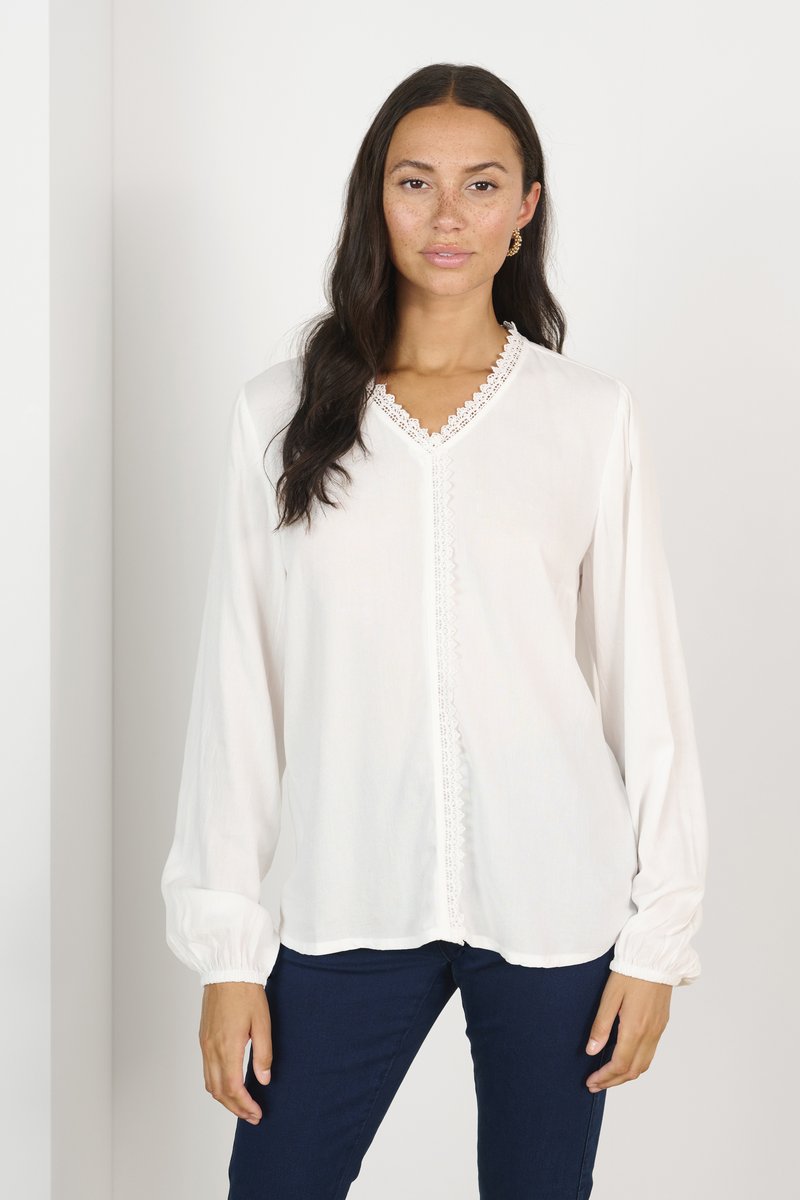 White long-sleeve blouse with a V-neck and lace trim, featuring button front and gathered cuffs. Worn with dark blue jeans.