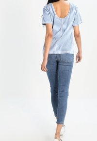 T-shirt à rayures bleu clair et blanche avec un dos en scoop, associé à un jean slim bleu foncé et des baskets blanches. Design simple, coupe confortable.