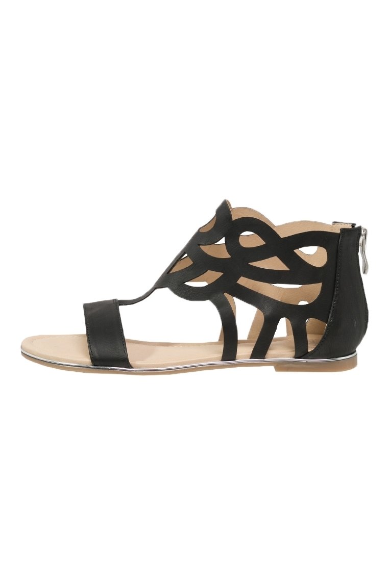 Svart sandal med intrikat utskärningsdesign, platt sula och dragkedja på baksidan. Har tunna remmar och beige innersula.