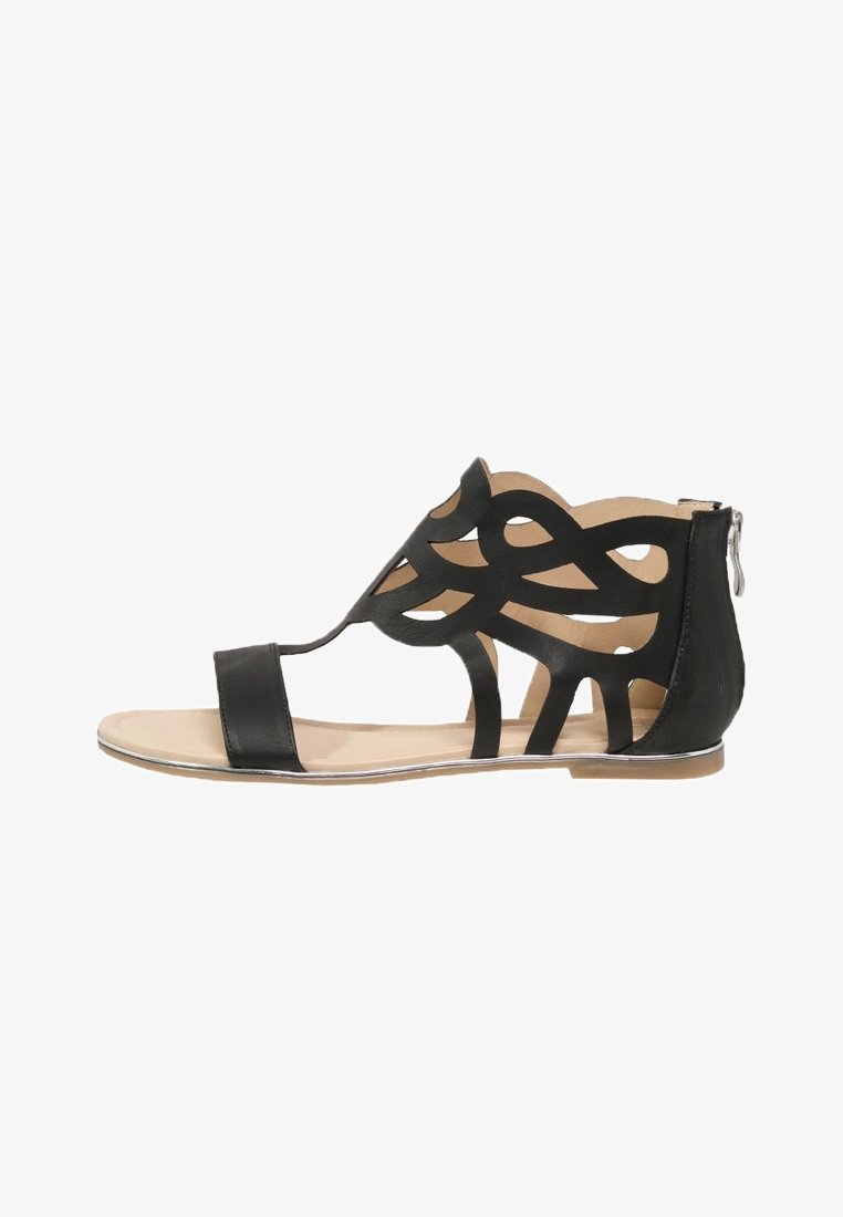 Svart sandal med intrikat utskärningsdesign, platt sula och dragkedja på baksidan. Har tunna remmar och beige innersula.