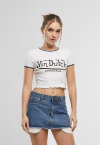 White cropped t-shirt with black "Von Dutch Originals" graphic, finished with a raw hem. Paired with a denim mini skirt featuring a distressed edge.