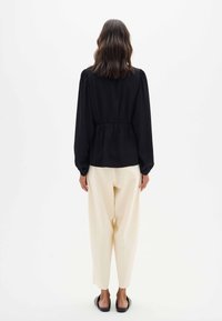Blusa negra con mangas abullonadas y cintura fruncida, combinada con pantalones crema. Diseño simple, tejido ligero y corte casual.