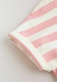 Manžeta kratkih rukava na tkanini s ružičastim i bijelim horizontalnim prugama, prikazujući teksturu pletenja i detalj presavijenog ruba.