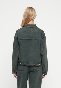 Denim jakna s temnim pranjem, z ovratnikom, dolgimi rokavi in snap gumbi na manšetah in robu. Ohlapen kroj.