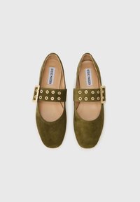 Green suede flat shoes with a rounded toe, featuring a wide strap with gold circular hardware and five gold eyelets.