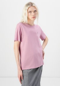 T-skjorte med kort erm og rund hals i myk lyserosa bomull med en liten logo på brystet og en avslappet passform. Stylet med grå cargo-bukser.