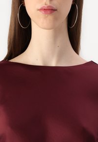 Burgundy top with a smooth texture and wide neckline, paired with large silver hoop earrings. Focus on the neck and shoulder area.