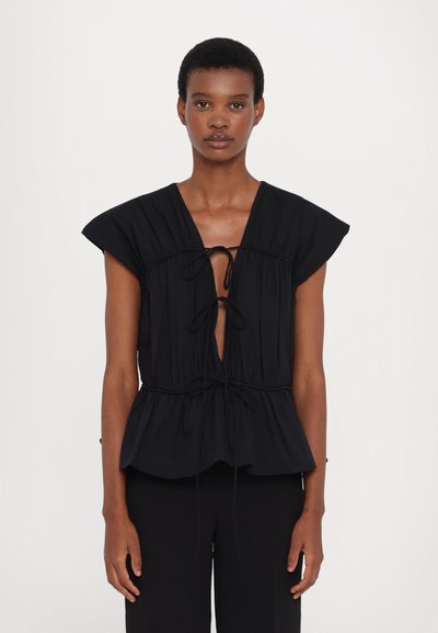 Blouse noire avec un décolleté en V profond et une taille froncée. Elle présente des manches courtes et un lien décoratif à nouer sur le devant, fabriquée en tissu doux.