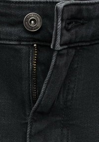 Vaqueros de mezclilla negra con cremallera y un botón metálico con la inscripción "MNG Denim". La tela tiene una textura suave y costuras mínimas.