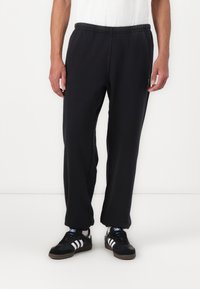 Black sweatpants with an elastic waistband, loose fit, and cuffed ankles; displayed with a white t-shirt and black sneakers.