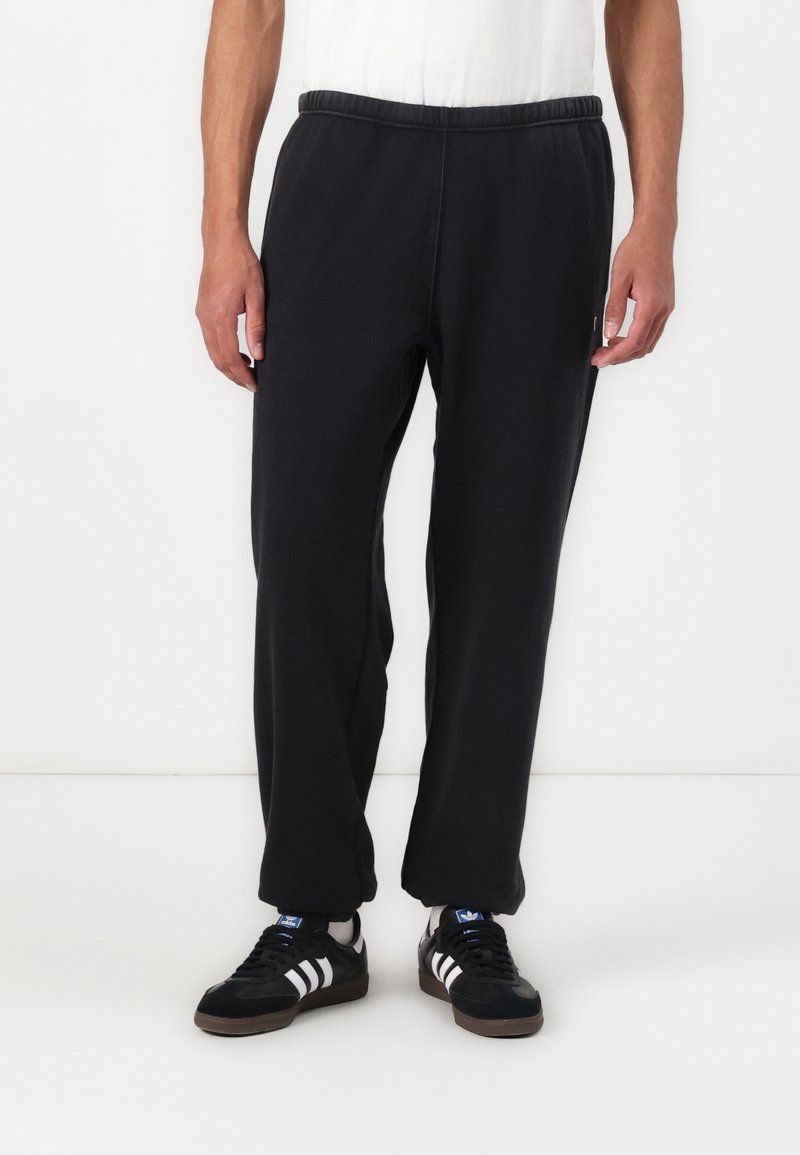 Black sweatpants with an elastic waistband, loose fit, and cuffed ankles; displayed with a white t-shirt and black sneakers.