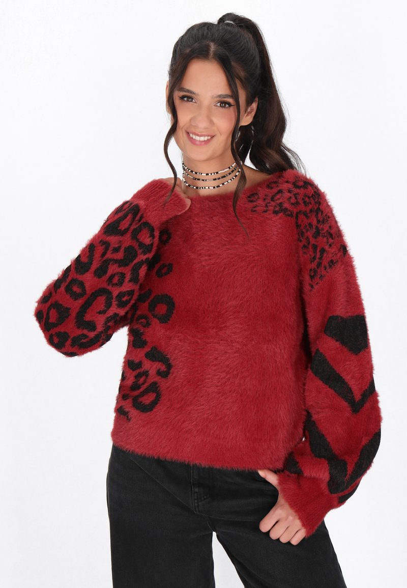 Maglione rosso in pelliccia sintetica con stampa animale nera sulle maniche, dal fit rilassato e ampio scollo. Abbinato a pantaloni neri.