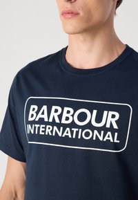 Ναυτικό μπλε βαμβακερό μπλουζάκι με μεγάλη λευκή εκτύπωση "BARBOUR INTERNATIONAL" στο μπροστινό μέρος, με κλασικό σχέδιο στρογγυλής λαιμόκοψης.