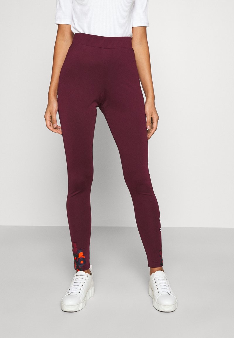 Maroon leggings with a high waistband, featuring floral print accents near the ankles. Made from stretchy fabric; paired with white sneakers.