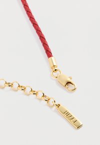 Czerwony pleciony skórzany pasek z złotym metalowym łańcuszkiem i zapięciem. Zawiera zawieszkę z napisem "LUVAJ" w złotym kolorze na prostokątnej charms.