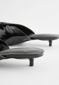 Černé lakované kožené nazouvací muly s minimalistickým designem, s nízkým stiletto podpatkem a hladkým povrchem. Výrazné logo na stélce.