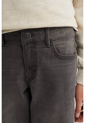 Jean gris foncé à la taille avec passants pour ceinture, poche avant et bouton fermé, porté avec un haut beige à manches longues et main visible sur le côté.