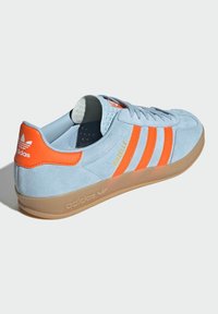 Adidas Gazelle sneakers in light blue suede with orange stripes and accents; features a gum sole and padded collar for comfort.