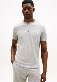 Szara bawełniana koszulka z krótkim rękawem, okrągłym dekoltem i logo "TOMMY HILFIGER" w białym i czerwonym kolorze na klatce piersiowej. Gładka tekstura, luźny krój.