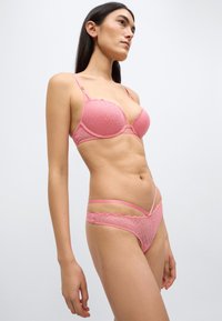 Σετ ροζ εσώρουχα που περιλαμβάνει ένα σουτιέν με ενίσχυση και λεπτομέρειες από δαντέλα με γεωμ ετρικά σχέδια, συνδυασμένο με τανγκό σετ με λεπτές τιράντες.