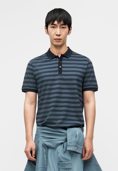 Polo rayé bleu marine et bleu clair à manches courtes, col et patte de boutonnage à trois boutons, superposé à un vêtement bleu clair.