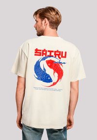 Beige oversized t-shirt featuring a red and blue koi fish graphic, bold red text, and a smooth cotton texture.