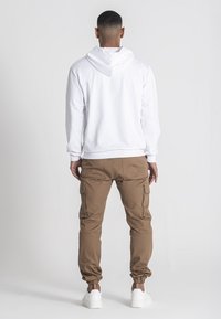 Sudadera blanca con capucha y cordones ajustables, junto con pantalones cargo marrones que cuentan con bolsillos laterales y puños elásticos.