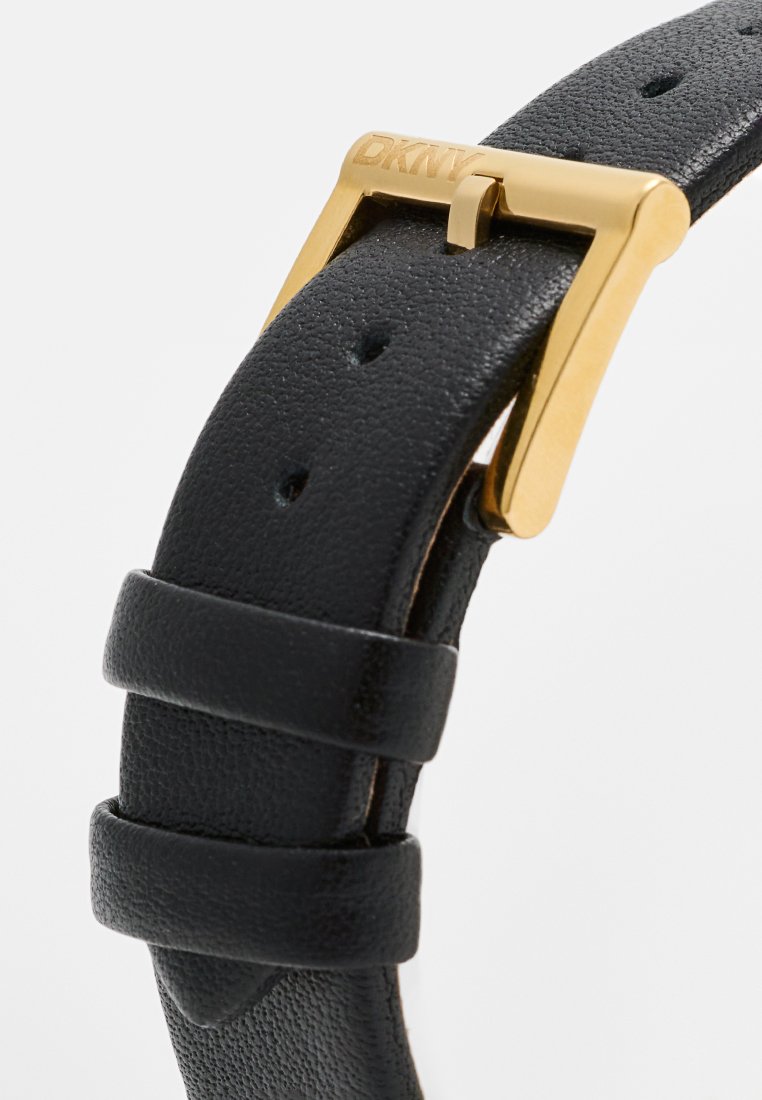 Schwarzes strukturiertes Lederarmband für Uhren mit einer goldenen Metallschnalle, die mit dem "DKNY"-Logo graviert ist. Es verfügt über mehrere Einstelllöcher und zwei Schlaufen.