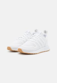 Zapatos deportivos blancos con parte superior de malla, tres rayas horizontales y suela de goma. Presenta un collar acolchado y cordones para un ajuste seguro.