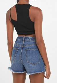 Svart ribbad kort t-shirt med en unik ryggdesign, i kombination med högmidjade blå jeansshorts med fransade kanter och bakfickor.