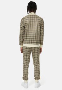 Rutet træningsdragt i beige, brun og gul. Blødt stof med ribbede manchetter, der har en afslappet pasform og elastisk talje. Hvide sneakers.
