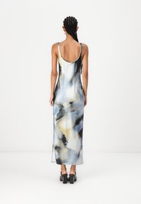 Rochie maxi dintr-un material fluid, cu un model abstract în culorile albastru, negru și galben, bretele subțiri și fante laterale, asortată cu pantofi cu toc pătrat.
