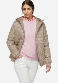 Beige gewatteerde jas met een capuchon, met een soepele textuur, staande kraag en een roze trui eronder, gecombineerd met witte broek.