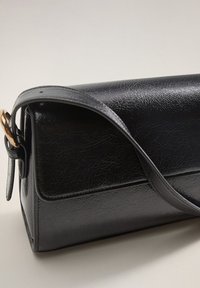 Musta keinonahkainen olkalaukku, jossa on rakenteellinen suorakulmainen muoto. Varustettu kullanvärisellä yksityiskohdalla ja sileällä pinnalla. Säädettävä hihna kiinnitettynä.