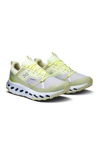 Baskets de sport vert clair et blanches avec un tissu en mesh, semelle épaisse, accents texturés et lacets jaunes vifs. Présente un logo sur le côté.