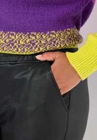 Maglione lavorato a maglia con parte superiore viola e orlo giallo a fantasia, abbinato a pantaloni in pelle nera, che mostrano una texture liscia e un design aderente.